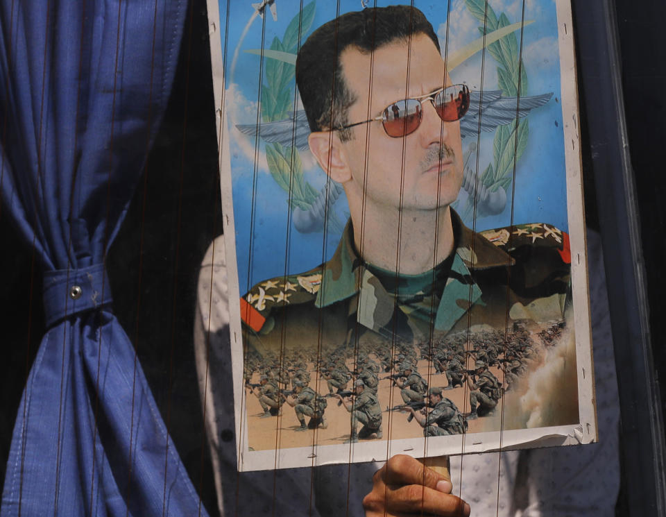 FILE - In this Aug. 13, 2018 file photo, a Syrian refugee holds a poster of President Bashar Assad in a bus window at the border crossing point of Jdedeh Yabous, on his way to Syria. Assad said Sunday, Feb. 17, 2019, that only the Syrian army can protect groups in northern Syria. In a speech in the Syrian capital Damascus on Sunday, he appeared to be referring to U.S.-allied Kurdish groups, which fear a Turkish assault once American troops withdraw from northeastern Syria. (AP Photo/Sergei Grits, File)