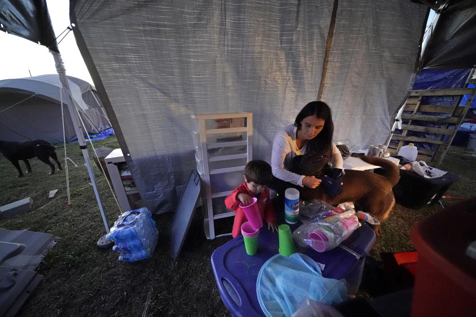 Cristin Trahan looks through supplies next to her grandson Ricky Trahan III, in an improvised kitchen area under a tarp, amidst the rubble of the family's destroyed home in Lake Charles, La., Friday, Dec. 4, 2020. They were hit by Hurricanes Laura and Delta. She, her husband and a son are living in tents on the property, while her son, his fiancée and their son Ricky III are living in a loaned camper there. A relatives home on the same property is now gutted and they are living in a camper as well. (AP Photo/Gerald Herbert)