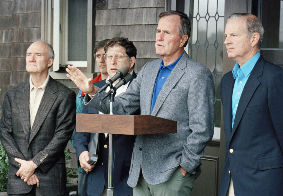 FILE - In this August 11, 1990 file photo, President George H. W. Bush comments to reporters at his Kennebunkport home in Maine, after meeting with his advisers on the Middle East crisis. Listening from left, are National Security Adviser Brent Scowcroft, White House Andy Card (partially hidden), Chief of Staff John Sununu, and Secretary of State James Baker III. A longtime adviser to Presidents Gerald Ford and George H.W. Bush has died. Brent Scowcroft was 95. A spokesperson for the late President Bush says Scowcroft died Thursday of natural causes at his home in Falls Church, Virginia.(AP Photo/Doug Mills)