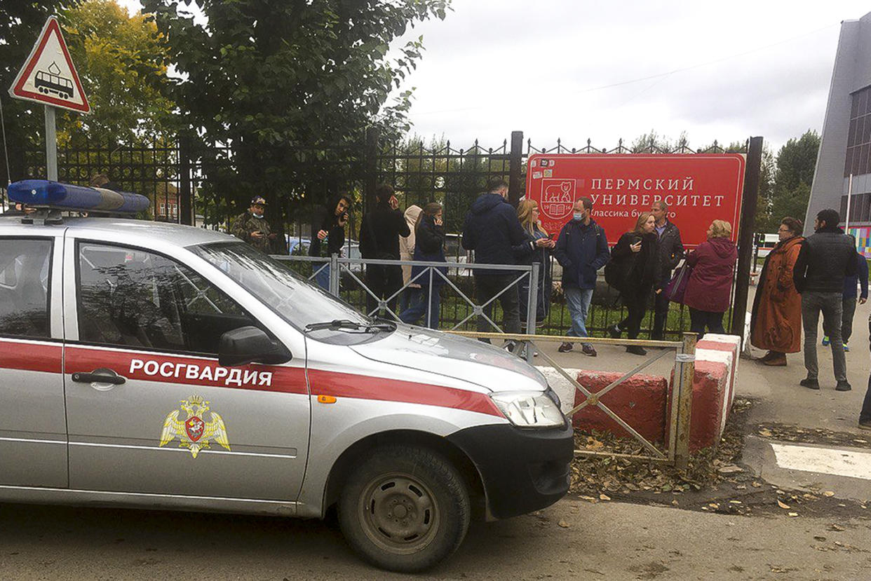 People stand behind the fence near Russia's Perm State University on Monday, Sept. 20, 2021, where a  gunman opened fire leaving at least 8 people dead and others wounded, according to Russia's Investigative Committee. (AP Photo/Anastasia Yakovleva)