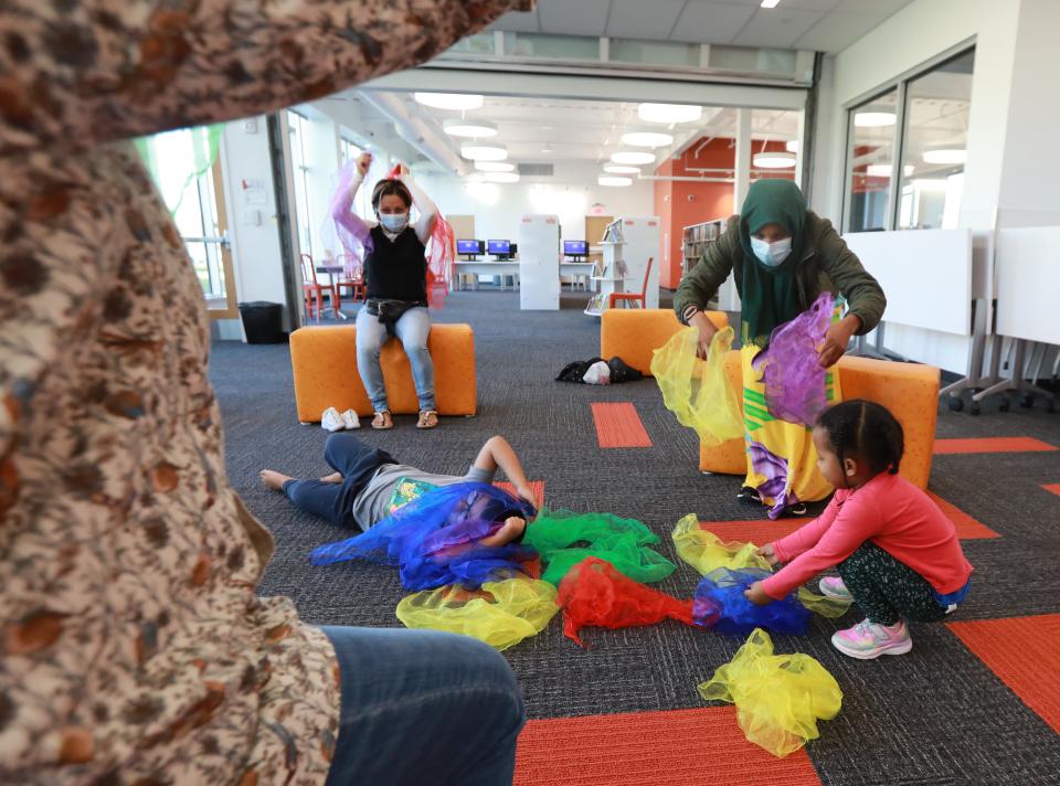 Mickie Stiers, left, the youth services manager at the Columbus Metropolitan Library's Karl Road Branch, frames parents Angelica Sanchez, center, and Amina Mohamed as their children play with scarves during a laptime story session. As the pandemic eases, some activities have resumed at library locations.