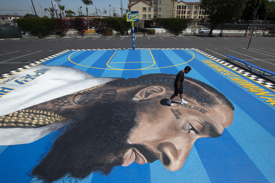 FILE - In this April 17, 2019 file photo, mural artist Gustavo Zermeno Jr. walks on a basketball court mural he dedicated to slain rapper Nipsey Hussle in Los Angeles. Hussle, 33, was shot and killed outside his Los Angeles clothing store on March 31, 2019. A year after Hussle's death, his popularity and influence are as strong as ever. He won two posthumous Grammys in January, he remains a favorite of his hip-hop peers and his death has reshaped his hometown of Los Angeles in some unexpected ways. (AP Photo/Jae C. Hong, File)