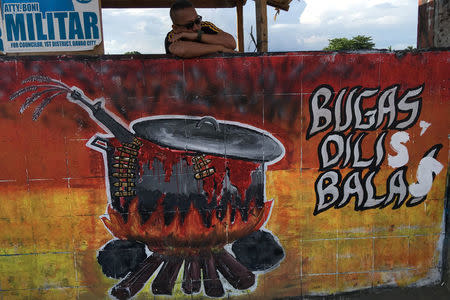 A security guard peers over a wall decorated with a gun in a cooking pot and the phrase "Rice not bullets" in Davao, Philippines May 15, 2016. REUTERS/Andrew RC Marshall