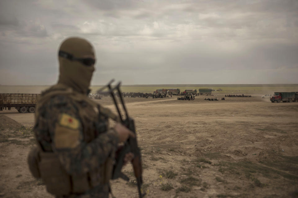 In this Wednesday, March 6, 2019, photo, a member of U.S.-backed Syrian Democratic Forces (SDF) stands guard at a reception area for people evacuated from the last shred of territory held by Islamic State militants, outside Baghouz, Syria. (AP Photo/Gabriel Chaim)