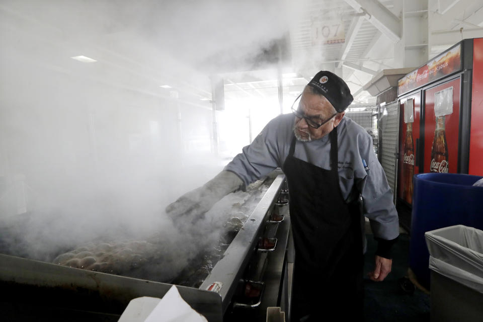 A sous chef, who declined to be identified, sends up a cloud of smoke as he cleans his ballpark concession grill after the cancellation of the sprint training baseball game between the Kansas City Royals and the Seattle Mariners Thursday, March 12, 2020, in Surprise, Ariz. Major League Baseball is delaying the start of its season by at least two weeks because of the coronavirus outbreak and has suspended the rest of its spring training game schedule. (AP Photo/Elaine Thompson)