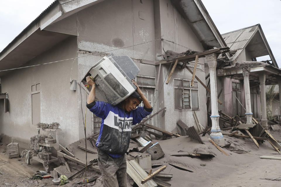 A man carries a television as he evacuates to a safer place following the eruption of Mount Semeru in Lumajang district, East Java province, Indonesia, Monday, Dec. 6, 2021. The highest volcano on Java island spewed thick columns of ash into the sky in a sudden eruption Saturday triggered by heavy rains. Villages and nearby towns were blanketed and several hamlets buried under tons of mud from volcanic debris. (AP Photo/Trisnadi)