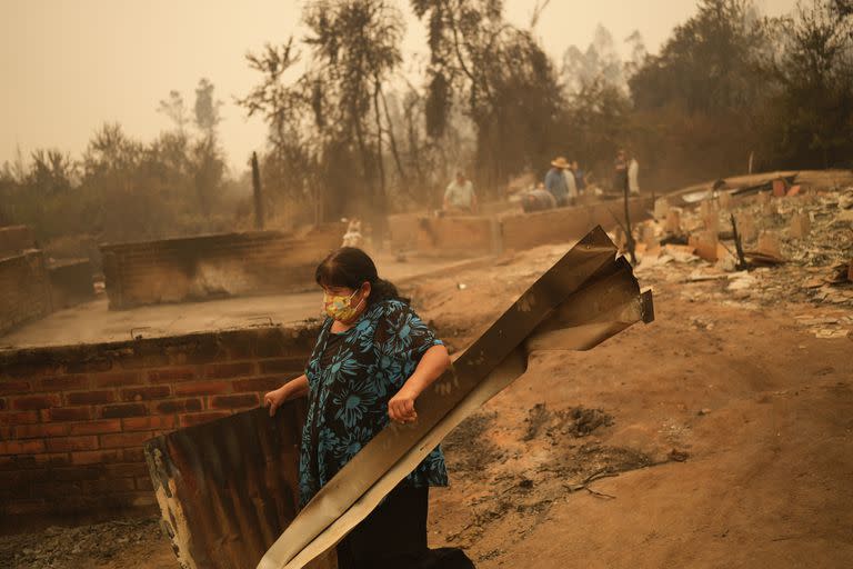 Una mujer remueve escombros en un paisaje devastado por el fuego en Santa Ana, Chile, sábado 4 de febrero de 2023. Al menos 23 personas han muerto en los incendios que han destruido viviendas y miles de hectáreas de bosques en el sur de Chile. (AP Foto/Matias Delacroix)