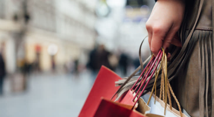 A close-up shot of a woman walking down the street with several paper shopping bags. retail stocks