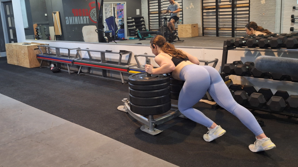 A woman pushes a sled in a gym