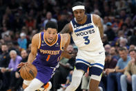 Phoenix Suns guard Devin Booker (1) drives past Minnesota Timberwolves forward Jaden McDaniels (3) during the second half of an NBA basketball game Wednesday, March 29, 2023, in Phoenix. The Suns won 107-100. (AP Photo/Ross D. Franklin)