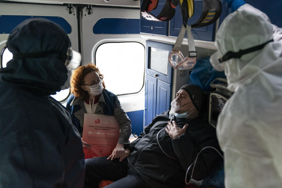 In this photo taken on Wednesday, May 6, 2020, ambulance medic Svetlana Padynich, right back to a camera, and an ambulance crew paramedic, left, observe a patient suspected of having coronavirus as his wife, second left, comforts him inside an ambulance on the way to a hospital in Chernivtsi, Ukraine. The hospital lacks a centralized oxygen supply and has to rely mostly on refillable oxygen masks, reflecting a pitiful state of Ukraine's underfunded health care system that was quickly overwhelmed by the coronavirus even with a relatively low number of infections. (AP Photo/Evgeniy Maloletka)