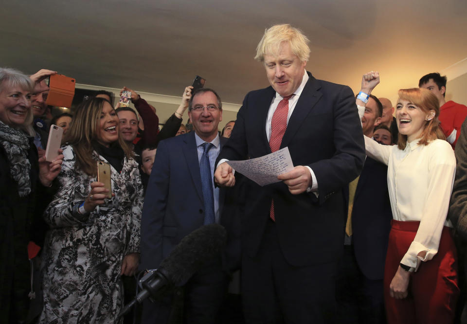 Britain's Prime Minister Boris Johnson reads from his notes as he speaks to supporters and new Sedgefield lawmaker Paul Howell, centre left, during a visit to meet newly elected Conservative party lawmakers at Sedgefield Cricket Club in County Durham, north east England on Saturday Dec. 14, 2019, following his Conservative party's general election victory. Johnson called on Britons to put years of bitter divisions over the country's EU membership behind them as he vowed to use his resounding election victory to finally deliver Brexit. (Lindsey Parnaby / Pool via AP)