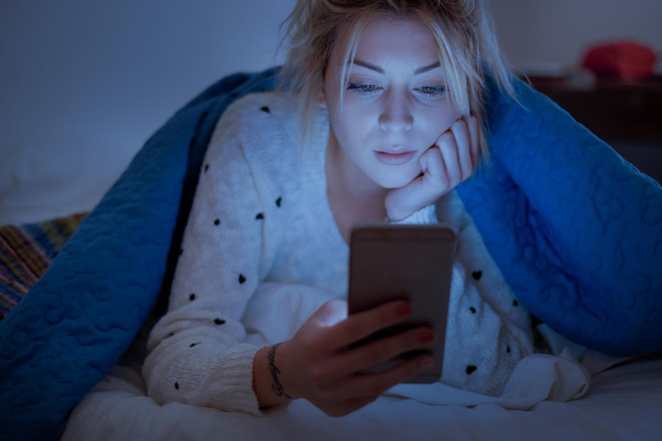 Disappointed sad woman holding mobile phone while laying on bed at night