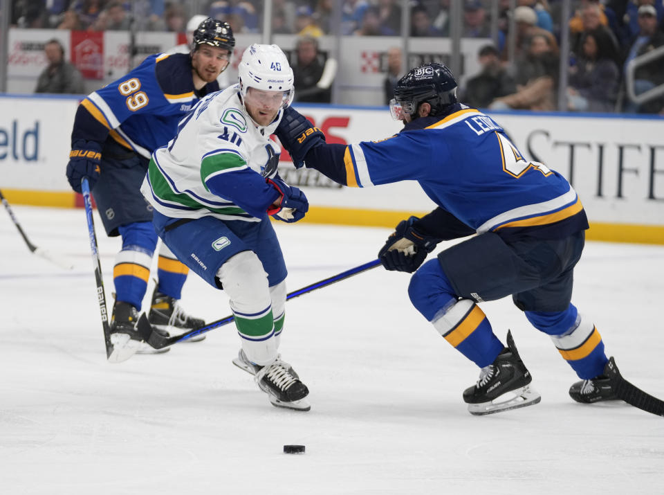 Vancouver Canucks' Elias Pettersson (40) and St. Louis Blues' Nick Leddy, right, battle for a loose puck during the third period of an NHL hockey game Tuesday, March 28, 2023, in St. Louis. (AP Photo/Jeff Roberson)
