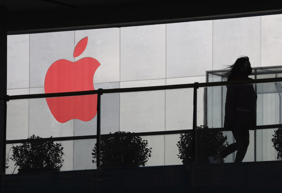 FILE - In this Dec. 6, 2018, file photo, a woman runs past a Apple logo colored red in Beijing, China. Apple is temporarily closing its 42 stores in mainland China, one of its largest markets, as a new virus spreads rapidly and the death toll there rose to 259 on Saturday, Feb. 1, 2020. The iPhone maker said in a statement it was closing stores, corporate offices and contact centers in China until Feb. 9 “out of an abundance of caution and based on the latest advice from leading health experts." (AP Photo/Ng Han Guan, File)