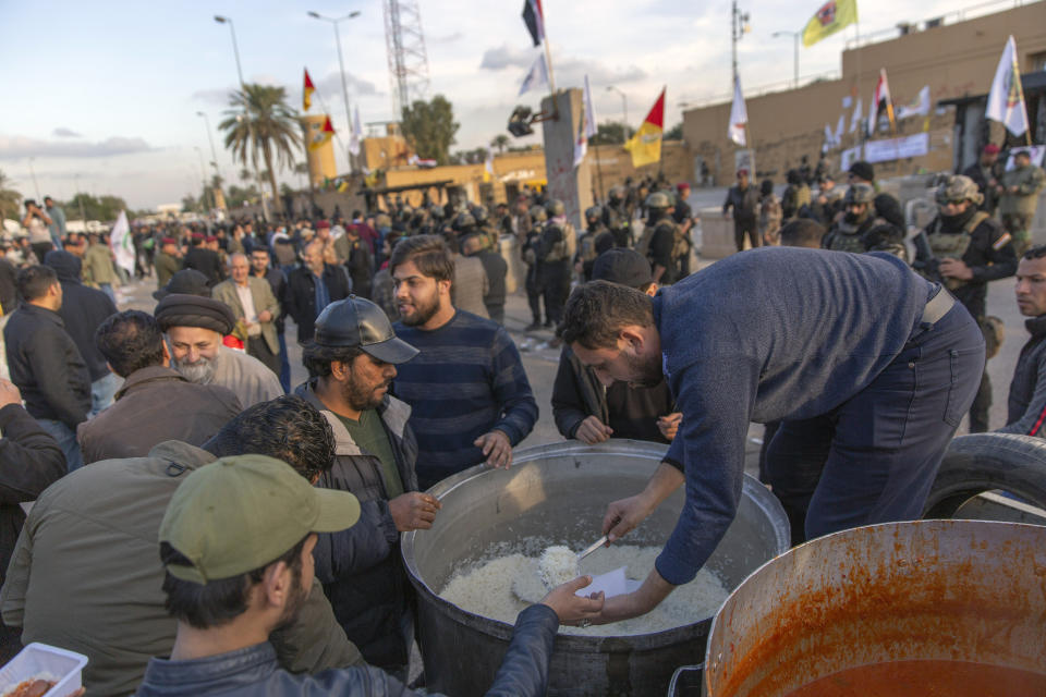 Pro-Iranian militiamen and their supporters receive free meals from the back of a truck while Iraqi army soldiers and security forces are deployed in front of the U.S. embassy, in Baghdad, Iraq, Wednesday, Jan. 1, 2020. Iran-backed militia have withdrawn from the U.S. Embassy compound in Baghdad after two days of clashes with American security forces. (AP Photo/Nasser Nasser)