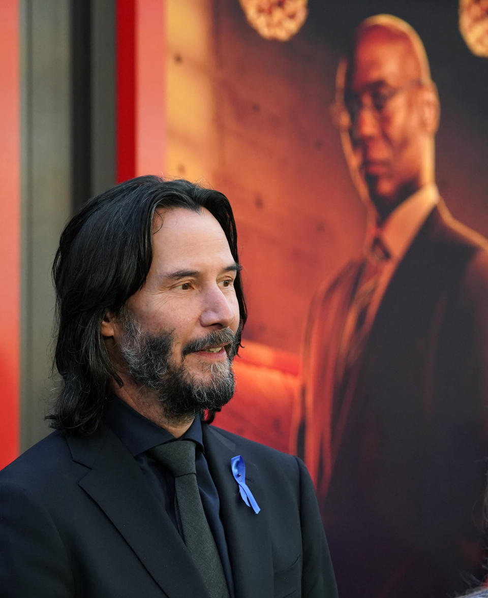 Keanu Reeves, the star of "John Wick: Chapter 4," wears a blue ribbon on his lapel in tribute to his late fellow cast member Lance Reddick, seen in a poster in the background, at the premiere of the film, Monday, March 20, 2023, at the TCL Chinese Theatre in Los Angeles. The veteran character actor Reddick died Friday morning at age 60. (AP Photo/Chris Pizzello)