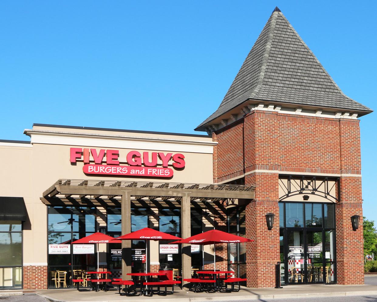 Front exterior of Five Guys Burgers and Fries restaurant in Nashville, Tennessee, doors and outdoor seating area with trees and a blue sky in the background