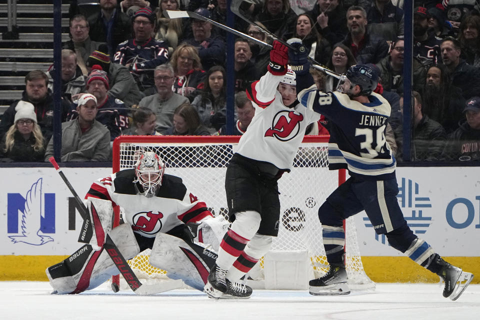 New Jersey Devils goaltender Vitek Vanecek, left, blocks a shot as defenseman Cal Foote, center, ties up Columbus Blue Jackets center Boone Jenner (38) in the first period of an NHL hockey game Friday, Jan. 19, 2024, in Columbus, Ohio. (AP Photo/Sue Ogrocki)