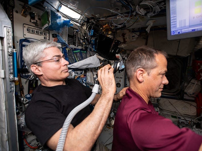 Vande Hei uses an electric razor with a vacuum attached that collects the hair he's cutting off fellow NASA astronaut Thomas Marshburn.