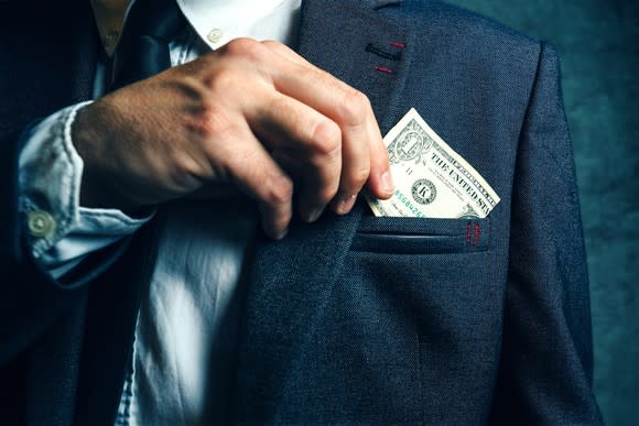 Man putting $1 bill in suit pocket.