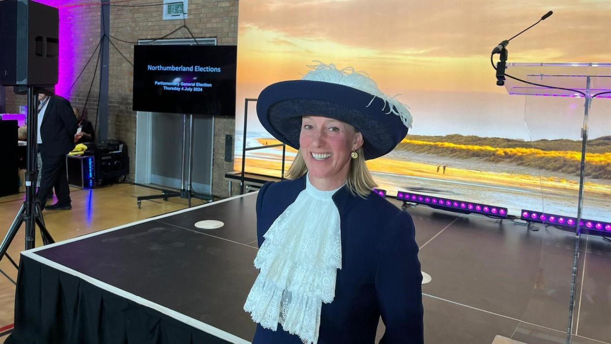 Lucia Bridgeman smiling at the camera, wearing her navy blue hat with white feathers