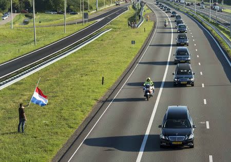 A man holds a Netherlands flag flying at half-mast (L) as a row of hearses carrying victims of the Malaysia Airlines flight MH17 plane disaster are escorted on highway A27 near Nieuwegein by military police, on their way to be identified by forensic experts in Hilversum, July 23, 2014. REUTERS/Marco de Swart