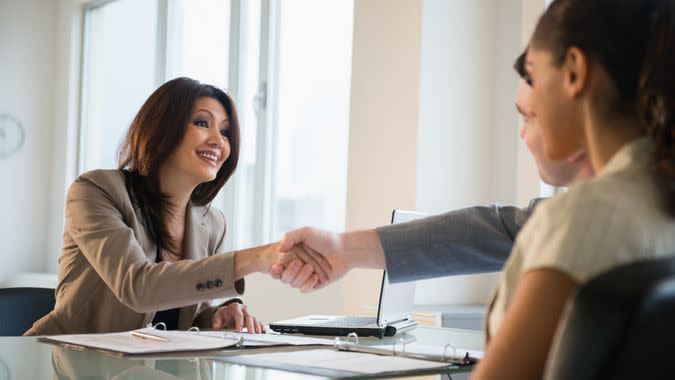 Businesswoman shaking hands with clients at desk.