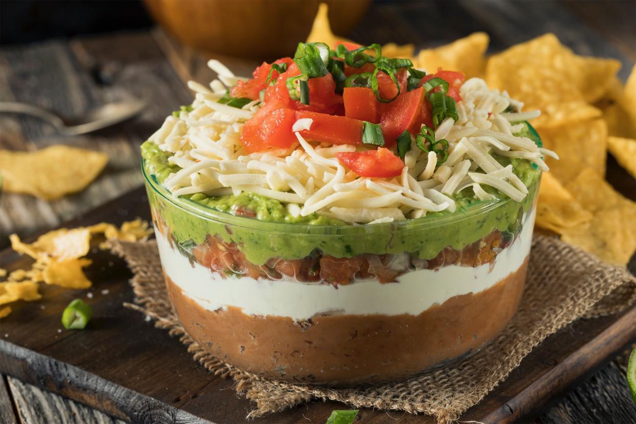 seven layer dip in a clear glass bowl with high sides, tortilla chips in background