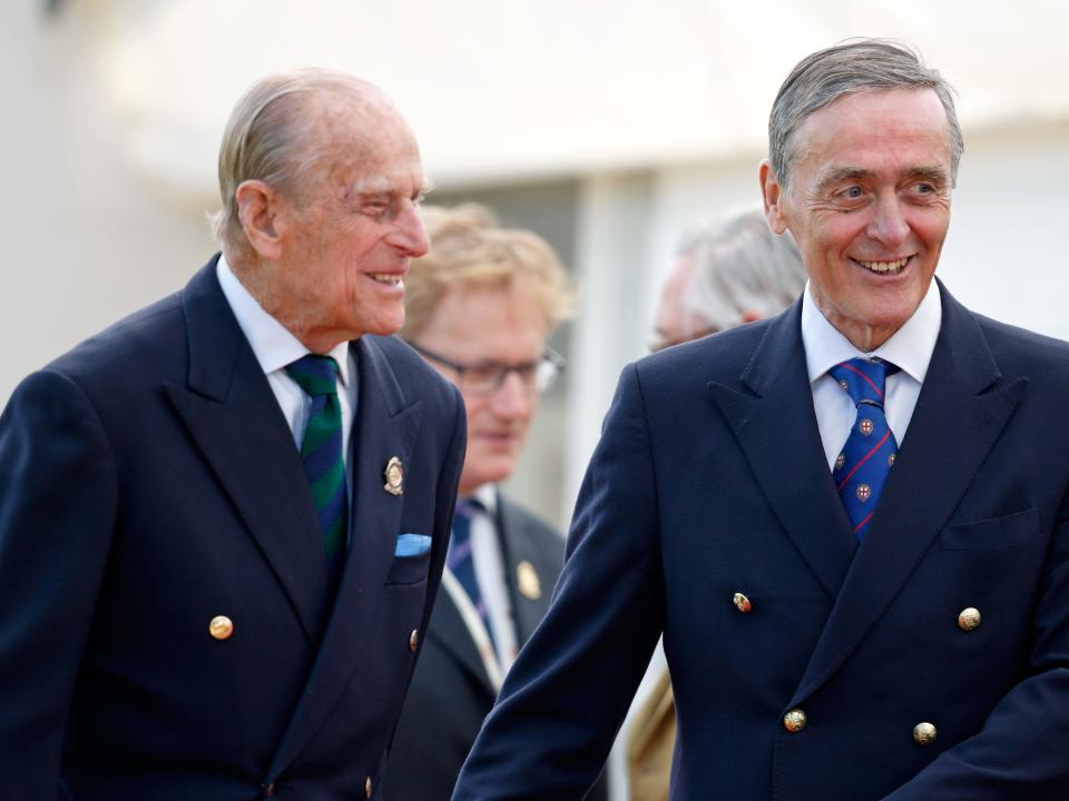 Gerald Grosvenor standing next to Prince Philip at a formal event where the two men are wearing blue suits and ties.