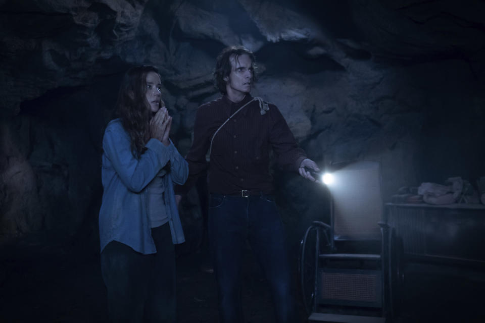 A shocked woman and a strange man explore a dark cavern with a flashlight