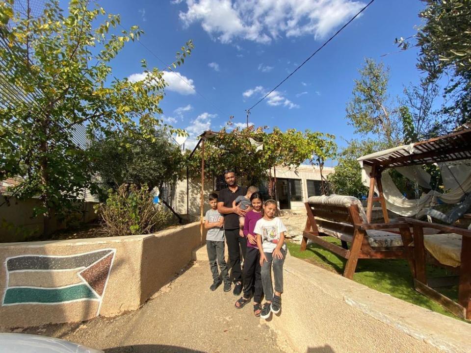 Sa'adat Gharib stands with his children at the entrance to their home in East Jerusalem, which is entirely surrounded by an Israeli settlement - and a high security fence - in mid-November 2023. / Credit: CBS News/Agnes Reau