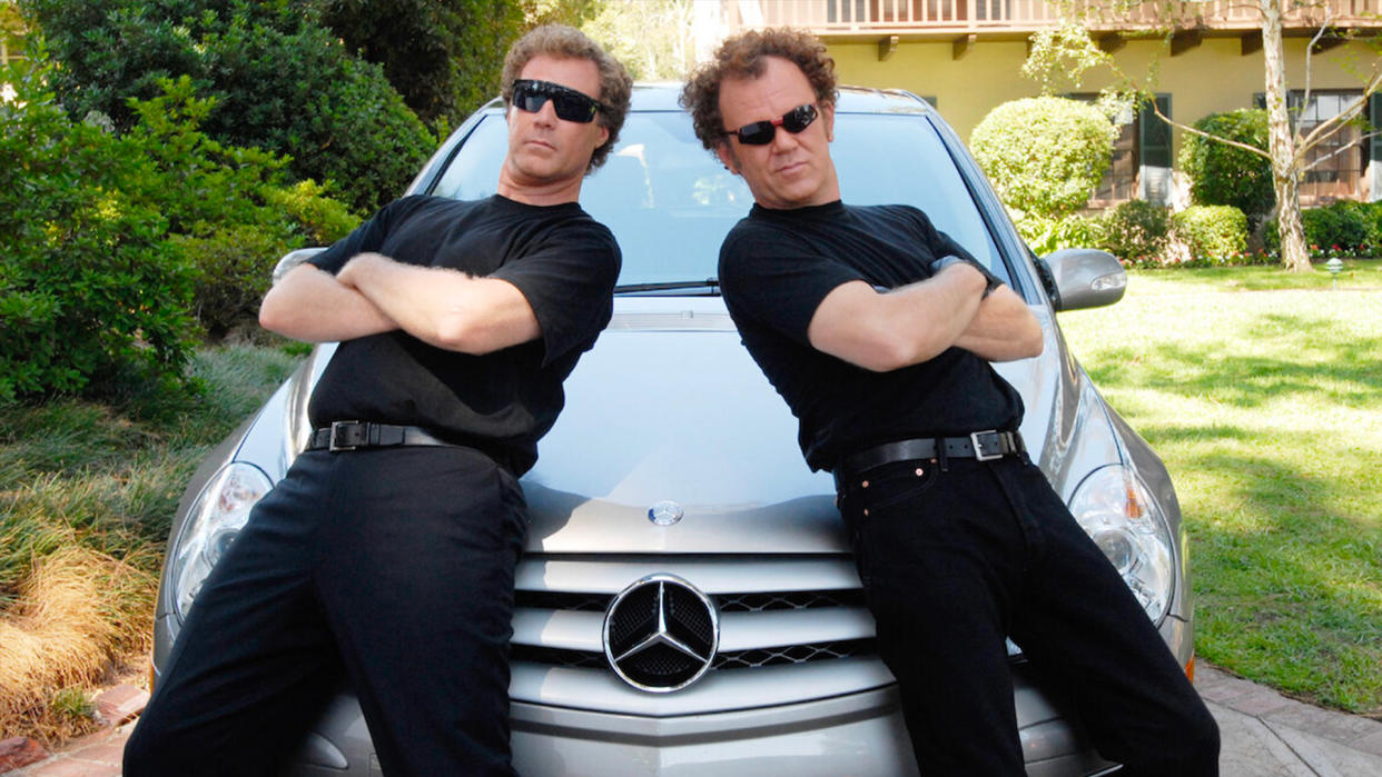  Will Ferrel and John C Reilly lean on the bonnet of a car while wearing glasse. 