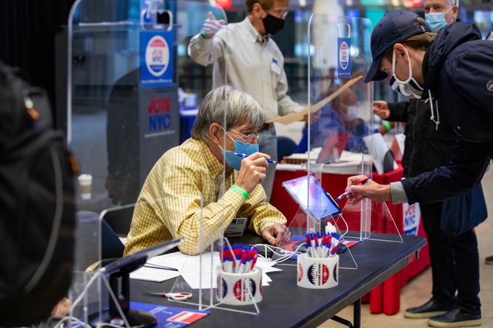 An election official wearing a protective mask assists a voter at an early polling location in Madison Square Garden, October 26, 2020.