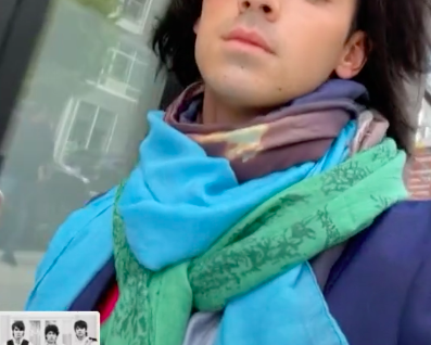 Joe is wearing several dark and light colored scarves with various prints