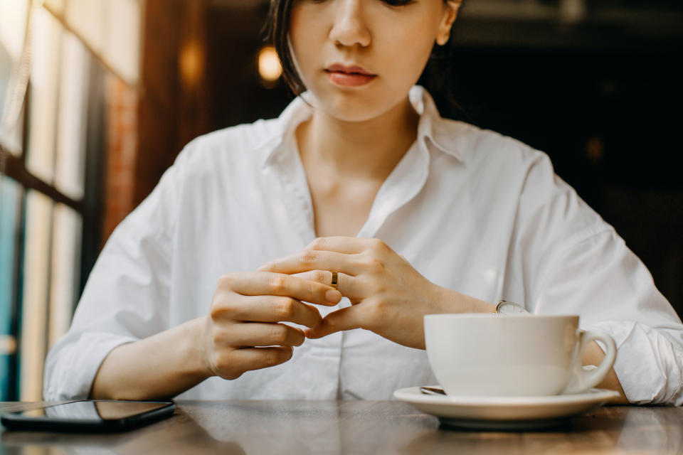 Woman touching the wedding ring on her finger nervously while having coffee and waiting in cafe