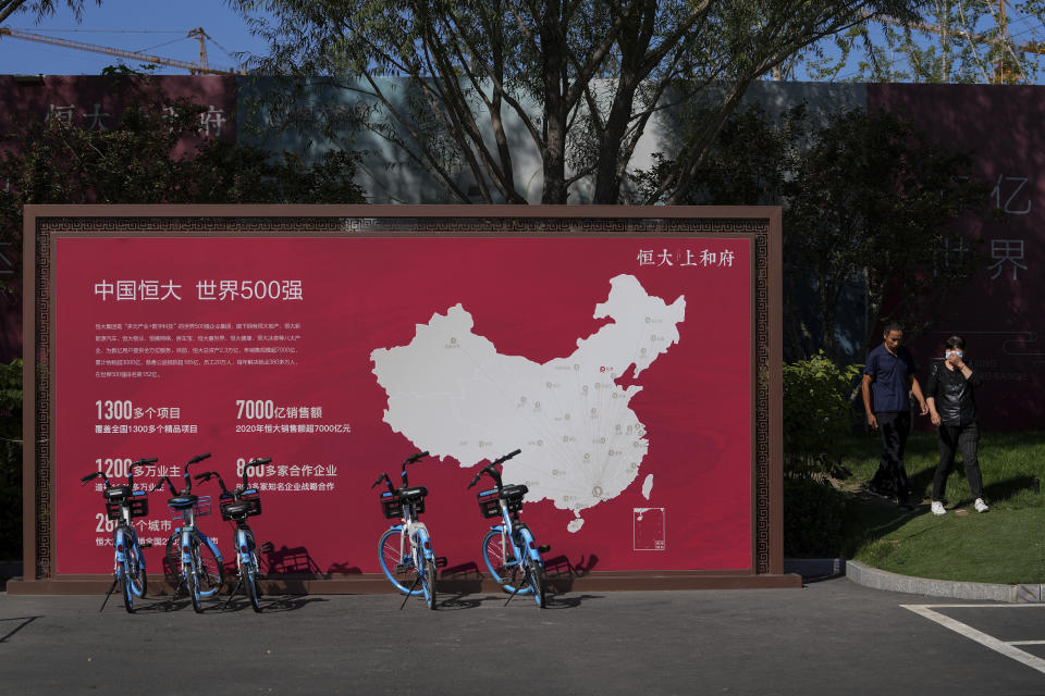 FILE - People walk by a map showing Evergrande development projects in China at an Evergrande new housing development in Beijing on Sept. 22, 2021. On Friday, Dec. 3, 2021, troubled Chinese developer China Evergrande Group, struggling under $310 billion in debt, warned it may run out of money to “perform its financial obligations,” sending regulators scrambling to reassure investors that China’s financial markets can be protected from a potential impact. (AP Photo/Andy Wong, File)