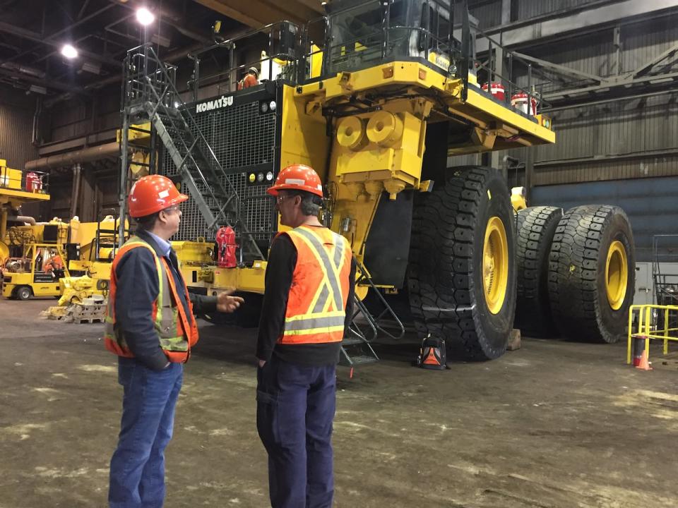 Two Tacora workers talk in front of a haul truck, which can hold about 250 tonnes of iron ore. The machine is so big, you can run over a pickup truck and not even notice.