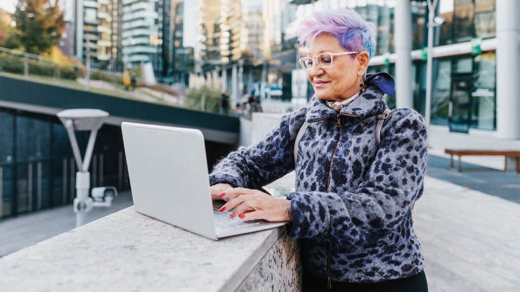 Older adult using a laptop on a wall in the street possibly researching the question is it mandatory to have Medicare deducted from social security