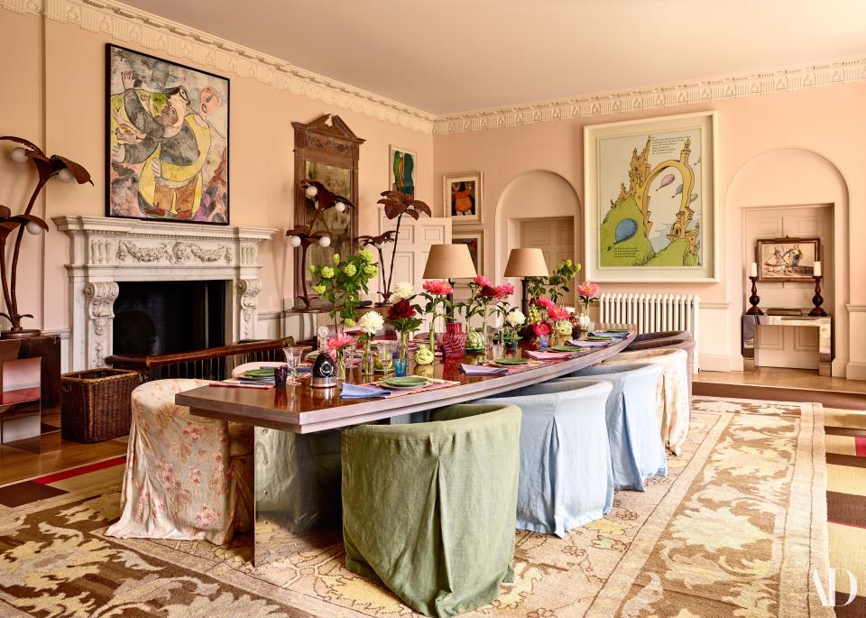 A custom table anchors the dining room of Brooke and Julian Metcalfe’s Oxfordshire home. A needlepoint rug lies atop a sisal carpet that Brooke painted with stripes. 1920s palm-tree lamps flank a painting by Albert Louden; flowers and glass vases from FLOWERBX; Tiffany & Co. plates.