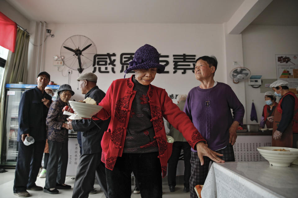 An elderly woman holds a bowl of vegetarian meal as others line up for their free lunch at Kang's canteen, the Harmonious and Happy Home, one of more than 80 operated by a charity for older people who live alone, in Dingxing, southwest of Beijing Thursday, May 13, 2021. China's leaders are easing limits on how many children each couple can have, hoping to counter the rapid aging of Chinese society.(AP Photo/Andy Wong)