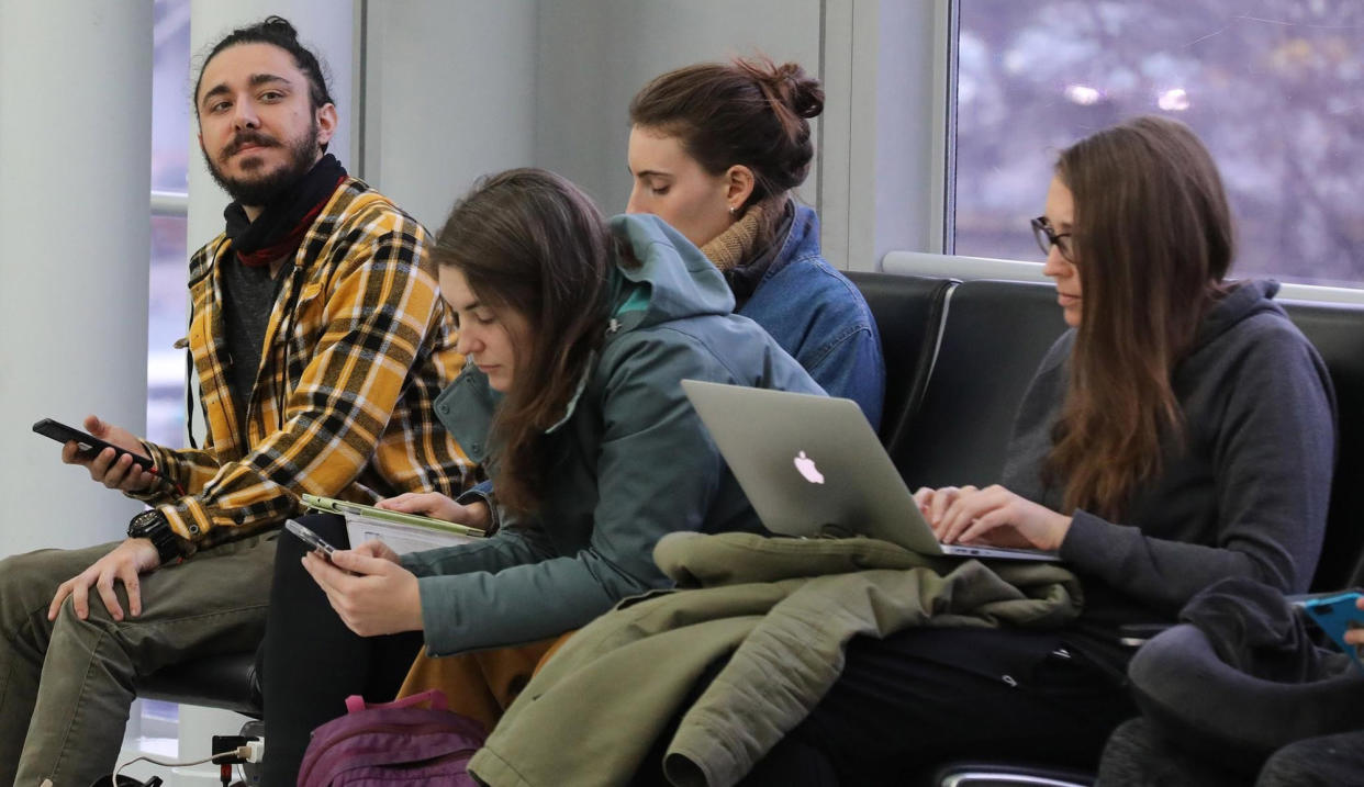 Mehmet Aytekin, 28, left, checks his cell phone while waiting to board his United Airlines flight to Newark, N.J. at O'Hare International Airport on Jan. 3, 2020.
