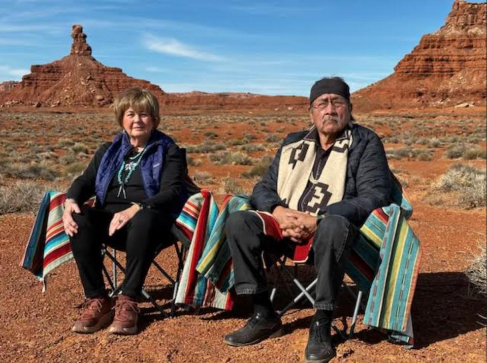 Zwei Menschen sitzen auf Stühlen in der Wüste unter blauem Himmel