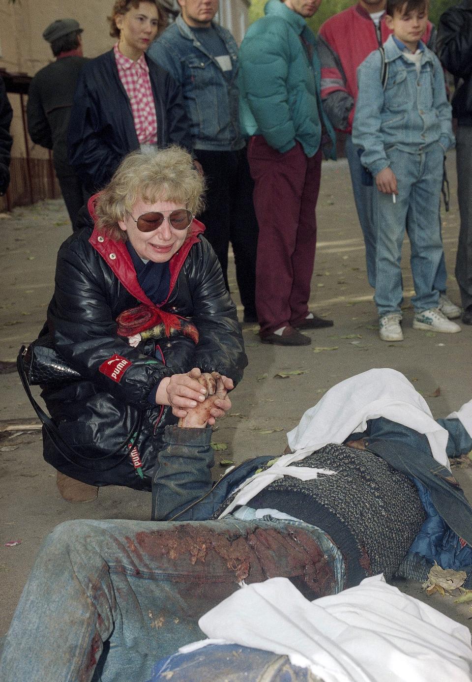 FILE - A woman weeps as she holds the hand of a man killed during the night near the Russian parliament building in Moscow, on Oct. 5, 1993. The October 1993 violent showdown between the Kremlin and supporters of the rebellious parliament marked a watershed in Russia's post-Soviet history. (AP Photo/Diether Endlicher, File)