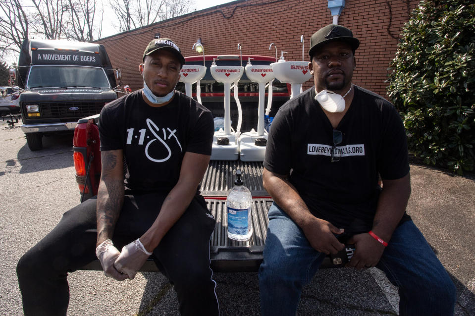 Grammy award-winning hip hop recording artist Lecrae, left, and Love Beyond Walls founder Terence Lester, right, sit on a truck bed filled with portable wash stations on Thursday, March 19, 2020 in College Park, Georgia. The wash stations were distributed by Lecrae and volunteers with Love Beyond Walls, a non-profit, throughout Atlanta in areas with a high density of homeless persons. (AP Photo/ Ron Harris)