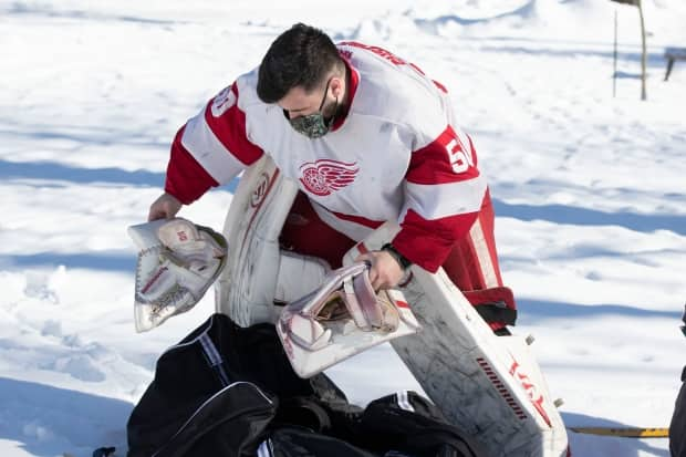 Calvin McLellan wears a mask while getting dressed to play hockey in Victoria Park in Kingston, Ont., Feb. 10, 2021, after the area moved into green on Ontario's COVID-19 scale.