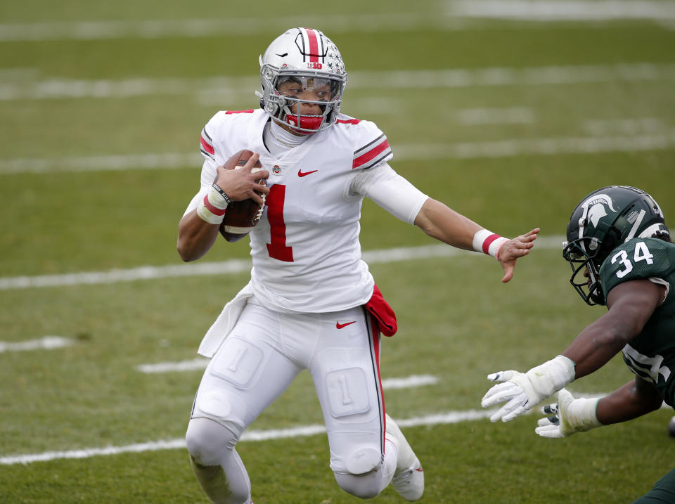 Ohio State quarterback Justin Fields, left, rushes against Michigan State's Antjuan Simmons during the first half of an NCAA college football game, Saturday, Dec. 5, 2020, in East Lansing, Mich.   (AP Photo/Al Goldis)