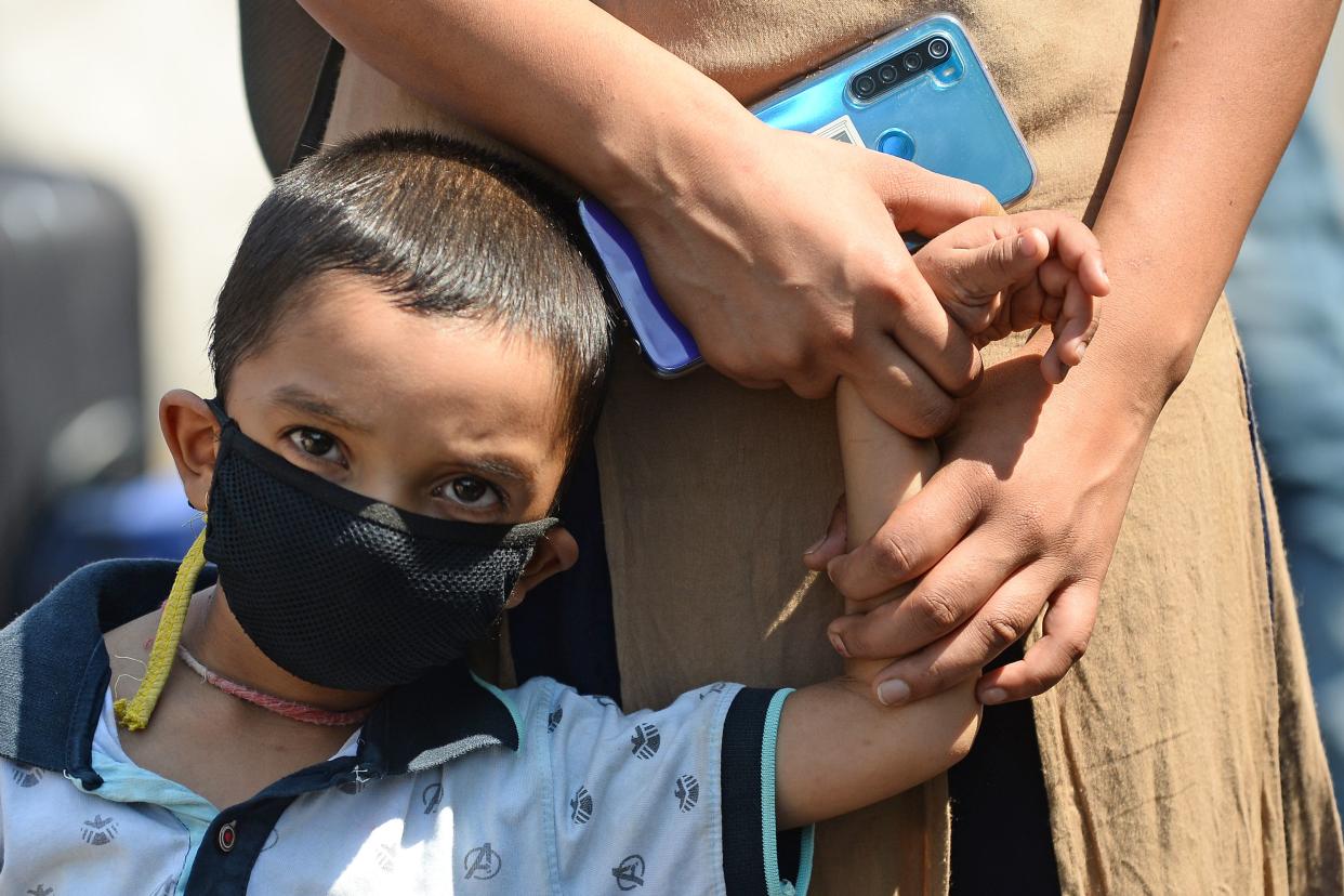 A child stands in a queue while holding hands of his mother outside the entrance of railway station in New Delhi on May 12, 2020. - India's enormous railway network was grinding back to life on May 12 as a gradual lifting of the world's biggest coronavirus lockdown gathered pace even as new cases surged. The country of 1.3 billion imposed a strict shutdown in late March, which Prime Minister Narendra Modi's government has credited with keeping cases to a modest 70,000, with around 2,000 deaths. (Photo by Sajjad HUSSAIN / AFP) (Photo by SAJJAD HUSSAIN/AFP via Getty Images)