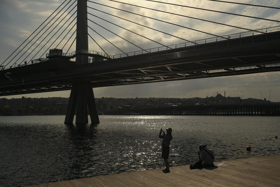 A woman takes a picture by the Golden Horn, leading to the Bosphorus Strait separating Europe and Asia, in Istanbul, Friday, May 14, 2021.Turkey is in the final days of a full coronavirus lockdown and the government has ordered people to stay home and businesses to close amid a huge surge in new daily infections. But millions of workers are exempt and so are foreign tourists. Turkey is courting international tourists during an economic downturn and needs the foreign currencies that tourism brings to help the economy as the Turkish lira continues to sink. (AP Photo/Emrah Gurel)