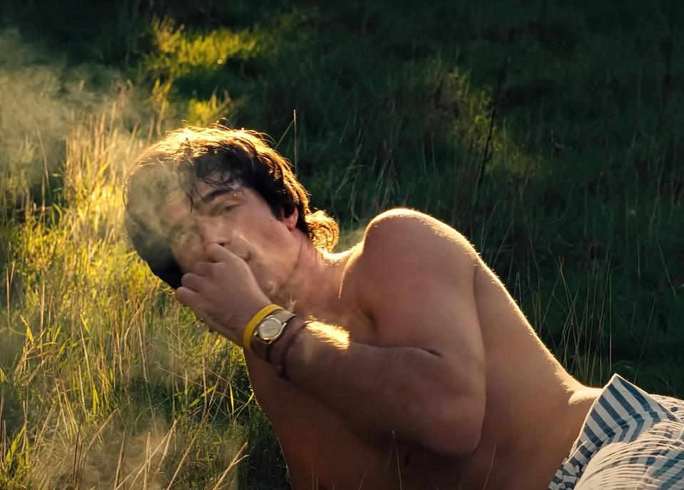 Jacob's character smoking why lying in the grass in a scene from "Saltburn"